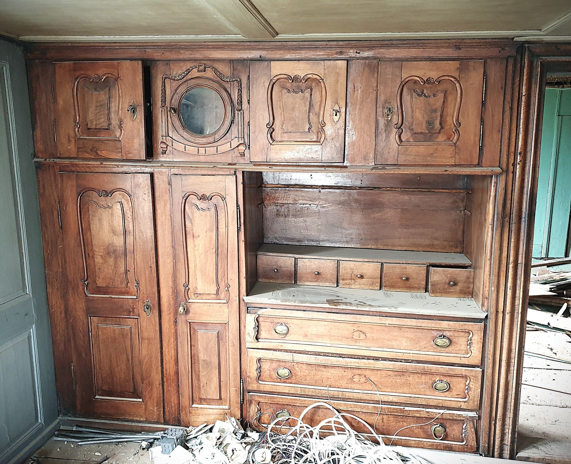 Geschnitzter Wandschrank mit Bullauge vor der Restauration, mit Bauschutt am Boden